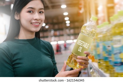 Young Beautiful Asian Woman Buying Vegetable Oil At Grocery Store, Happy Smile Wearing Green Sweater.