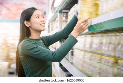 Young Beautiful Asian Woman Buying Vegetable Oil At Grocery Store, Wearing Green Sweater.