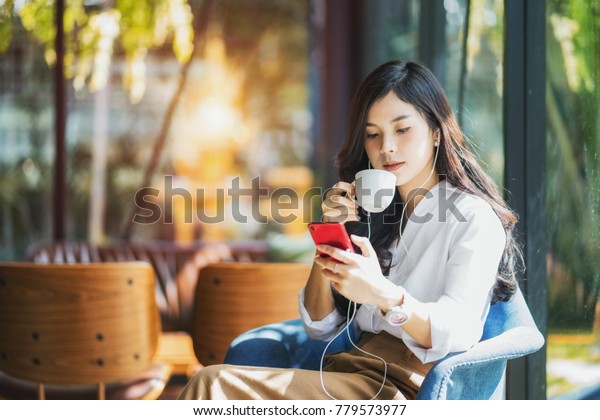 カフェで幸せにくつろいでいる間に 目を閉じ スマートフォンで音楽を聴く若い美しいアジア人女性 の写真素材 今すぐ編集