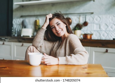 Young beautiful asian woman in cozy sweater sitting with cup of tea at table on kitchen at home - Powered by Shutterstock