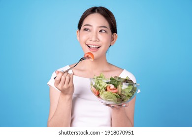 Young Beautiful Asian Woman Eating A Salad, Isolated On Blue Background.