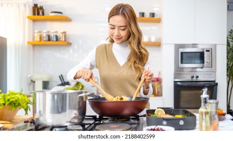 Young Beautiful Asian Woman Enjoy Cooking Healthy Food And Pasta In Cooking Pan On Stove In The Kitchen At Home. Happy Female Having Dinner Meeting Party Celebration With Friends On Holiday Vacation.