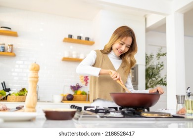 Young Beautiful Asian Woman Enjoy Cooking Healthy Food And Pasta In Cooking Pan On Stove In The Kitchen At Home. Happy Female Having Dinner Meeting Party Celebration With Friends On Holiday Vacation.