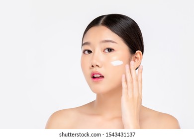 Young beautiful Asian woman with fresh clean appearance applying cream to face isolated on white background for beauty and skin care concepts