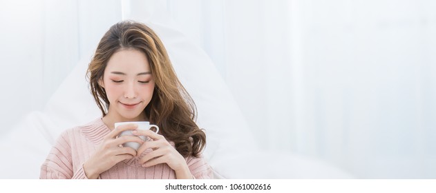 Young Beautiful Asian Woman Her Hands Holding A Cup Of Coffee Morning Winter Time In Her White Bedroom. Happy Cheerful Relaxing In Cold Winter, Barista Concept Banner