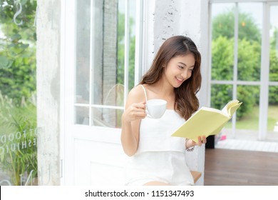 Young Beautiful Asian Woman Holding Coffee And Book With Attractive Smiling At Home. People Lifestyle Concept.