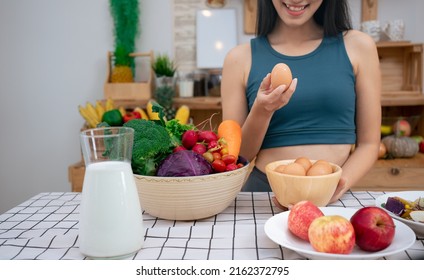 Young Beautiful Asian Woman Holding Organic Fresh Egg At Home With Surprise Face.Woman Taking Eggs.Healthy Food Nutrition Super Food.Sport Girl In Yoga Sport Wear Eat Breakfast In Home Kitchen. 