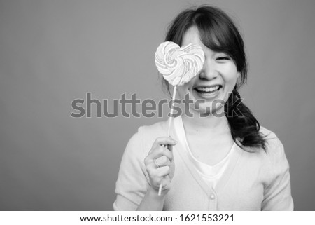 Young beautiful Asian woman holding heart shaped lollipop