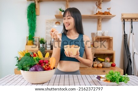 Young beautiful Asian woman holding organic fresh egg at home with surprise face.Woman taking eggs.Healthy food nutrition super food.Sport girl in yoga sport wear eat breakfast in home kitchen. 