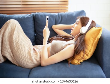 Young Beautiful Asian Woman Listening To Music With Headphones Relaxing On The Sofa. Chill Out And Leisure Concept