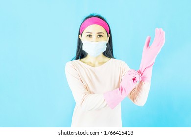 Young Beautiful Asian Woman Maid Wearing Face Mask  And Setting Up The Latex Gloves ,Isolated On Blue Background,Cleaning Service,housework And Household Concept.