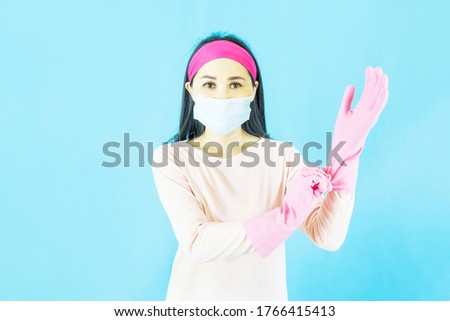 Young Beautiful Asian woman maid wearing face mask  and setting up the latex gloves ,Isolated on blue background,Cleaning Service,housework and household concept.