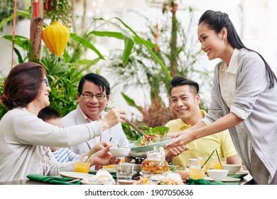 Young beautiful Asian woman offering tasty salad to guests at family dinner - Powered by Shutterstock