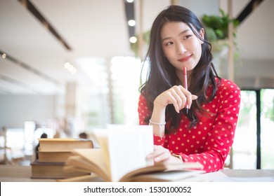 Young Beautiful Asian Woman Reading A Book While Doing Her Homework In The Modern Co Working Space