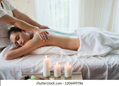 Young beautiful Asian woman relaxing in the spa massage and having salt scrub massage at back. healthy lifestyle and relaxation concept. Select focus hand of masseuse