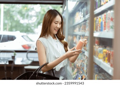 Young beautiful Asian woman shopping and choosing items in supermarket. Female white collar worker picking something to drink at convenient store