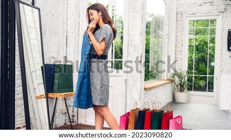 Young beautiful asian woman shopping and choosing clothes looking to mirror in the shop at fashion store with colorful shopping bag.fashion shopping concept