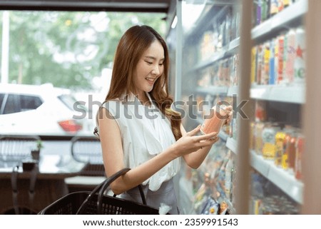 Young beautiful Asian woman shopping and choosing items in supermarket. Female white collar worker picking something to drink at convenient store