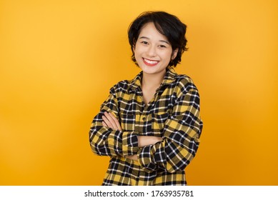 Young beautiful Asian woman with short hair wearing casual plaid shirt over yellow background happy face smiling with crossed arms looking at the camera. Positive person.