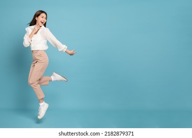 Young beautiful asian woman with smart casual cloth jumping and smiling with excitement looking at copy space isolated on blue background - Shutterstock ID 2182879371