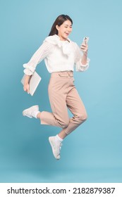 Young Beautiful Asian Woman With Smart Casual Cloth Use Smartphone And Jump Isolated On Blue Background