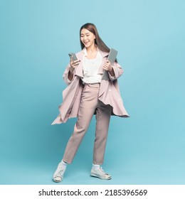 Young beautiful asian woman with smart casual cloth wearing pink coat smiling holding smartphone and laptop isolated on blue background - Shutterstock ID 2185396569