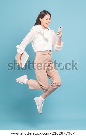 Young beautiful asian woman with smart casual cloth use smartphone and jump isolated on blue background