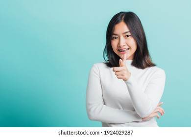 Young beautiful Asian woman smiling point finger at you with a confident expression, Portrait female pointing finger gesture towards you, studio shot isolated on a blue background
