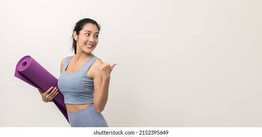 Young Beautiful Asian Woman With Sportswear Holding Yoga Mat On Pointing To Blank Space Isolated Background. Portrait Sporty Woman Standing Pose Exercise Workout In Studio. Training Yoga Lifestyle.