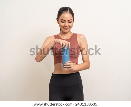 Young beautiful asian woman in sportswear holding bottle of water on isolated background. Portrait happy healthy slim fit and firm latin attractive sporty woman drinking water after exercise workout