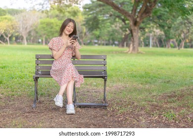 Young and beautiful Asian woman using her smartphone while resting in the park - Powered by Shutterstock