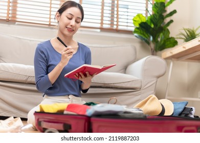 Young Beautiful Asian Woman Using Checklist Prepare Arrange Clothes And Equipment Before Go Travel Oversea After Covid Pandemic. New Normal Travel Lifestyle Concept.