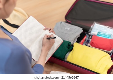 Young Beautiful Asian Woman Using Checklist Prepare Arrange Clothes And Equipment Before Go Travel Oversea After Covid Pandemic. New Normal Travel Lifestyle Concept.