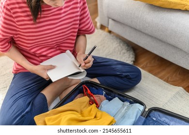 Young Beautiful Asian Woman Using Checklist Prepare Arrange Clothes And Equipment Before Go Travel Oversea After Covid Pandemic. New Normal Travel Lifestyle Concept.