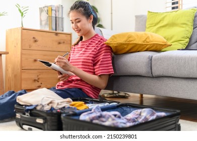 Young Beautiful Asian Woman Using Checklist Prepare Arrange Clothes And Equipment Before Go Travel Oversea After Covid Pandemic. New Normal Travel Lifestyle Concept.