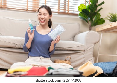 Young Beautiful Asian Woman Using Checklist Prepare Arrange Clothes And Covid Prevention Alcohol Spray Face Mask Before Go Travel Oversea After Covid Pandemic. New Normal Travel Lifestyle Concept.