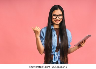 Young Beautiful Asian Woman Using Tablet Gadget Ipad Computer. Lifestyle Concept. Isolated On Pink Background. Pointing Finger Away.