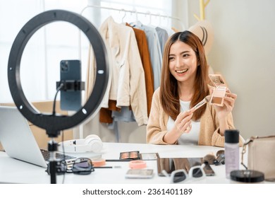 Young beautiful asian woman vlogger live broadcasting cosmetic makeup tutorial content with brush on looking at cell phone. Influencers with various cosmetic recording review video sharing on social - Powered by Shutterstock