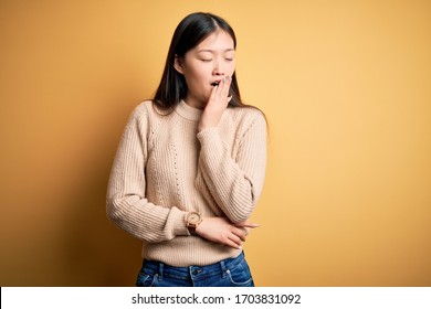 Young beautiful asian woman wearing casual sweater over yellow isolated background bored yawning tired covering mouth with hand. Restless and sleepiness.