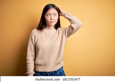 Young Beautiful Asian Woman Wearing Casual Sweater Over Yellow Isolated Background Confuse And Wondering About Question. Uncertain With Doubt, Thinking With Hand On Head. Pensive Concept.