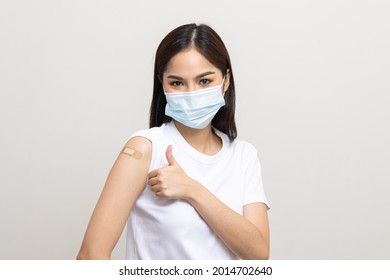 Young Beautiful Asian Woman Wearing Mask And Getting A Vaccine Protection The Coronavirus. Happy Female Showing Arm With Bandage After Receiving Vaccination On Isolated White Background.