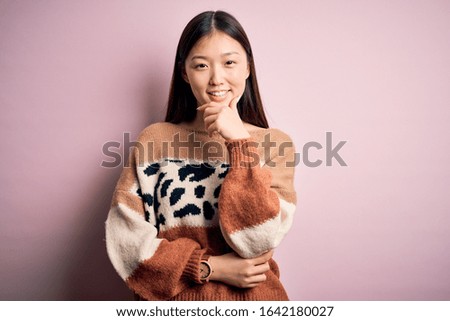 Young beautiful asian woman wearing animal print fashion sweater over pink isolated background looking confident at the camera smiling with crossed arms and hand raised on chin. Thinking positive.