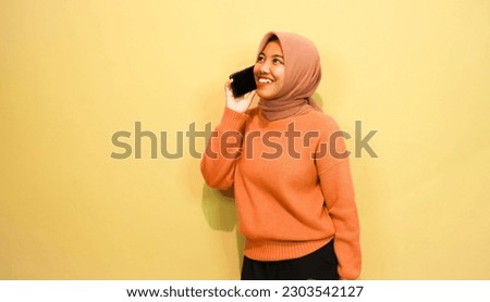 Young beautiful asian woman wearing orange sweater use smartphone isolated on orange background