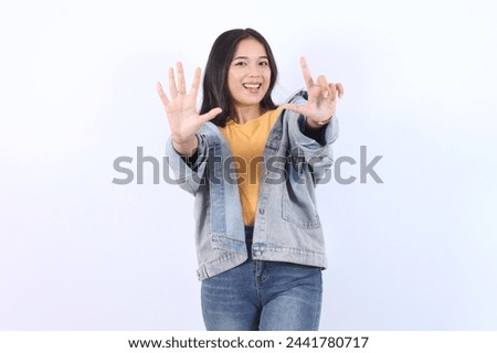 Young beautiful Asian woman wearing blue jacket yellow t-shirt showing number 7 and pointing up with finger number seven isolated on white background 