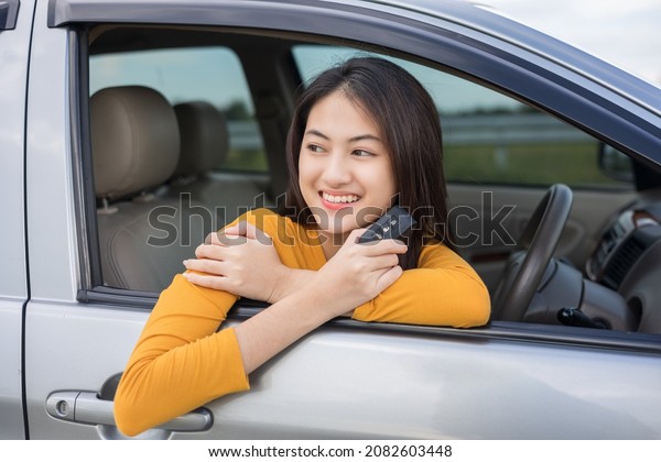 Young\
beautiful asian women getting new car. she very happy and excited\
looking outside window in hand holding car key. Smiling female\
driving vehicle on the road on a bright\
day
