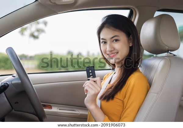 Young\
beautiful asian women getting new car. she very happy and excited\
looking outside window in hand holding car key. Smiling female\
driving vehicle on the road on a bright\
day