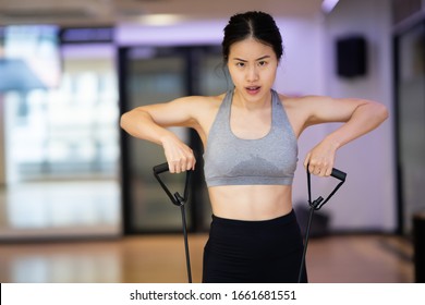 Young Beautiful Asian Women Workout At The Gym Indoor. She Is Using The Elastic Band To Stretch Her Arms And Legs. She Is Wearing Gym Clothes Grey Bra Outfit And Get Sweaty.