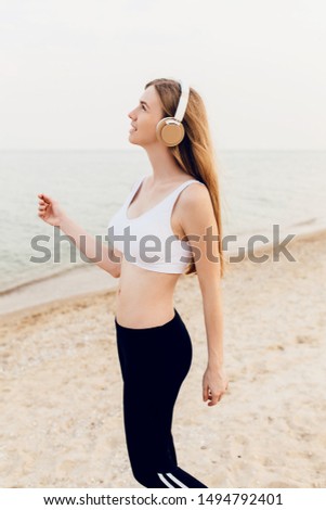Young beautiful athletic girl walking on the sea and listening to music after training