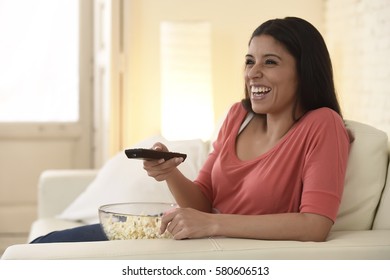 Young Beautiful And Attractive Hispanic Woman At Home Sofa Couch Laughing And Smiling Happy Watching Television Comedy Movie Or Funny Tv Series Alone Expressive Face Emotion Holding Remote