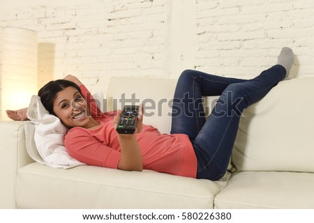 young beautiful and attractive latin woman at home sofa couch laughing and smiling happy watching television comedy movie or funny tv series alone expressive face emotion